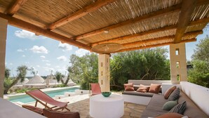Un área de estar al aire libre techada, con piscina, suelo de piedra y vistas del paisaje circundante.