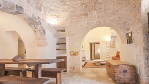 Una habitación rústica con paredes de piedra, un banco de madera, una mesa y un aparador.