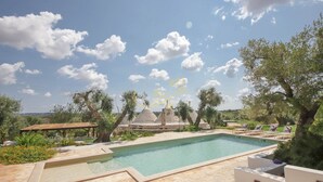 Piscina con deck de piedra, rodeada de árboles y una pérgola.