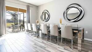 A modern dining area with a large table and chairs, a glass door leading to an outdoor patio, and two wall-mounted mirrors. - Solterra 12bd 11 5bat Sleeps24 Disney Pool Spa (Davenport)
