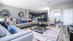 A modern living room with a sofa, coffee table, and a kitchen area in the background. - Solterra 12bd 11 5bat Sleeps24 Disney Pool Spa (Davenport)