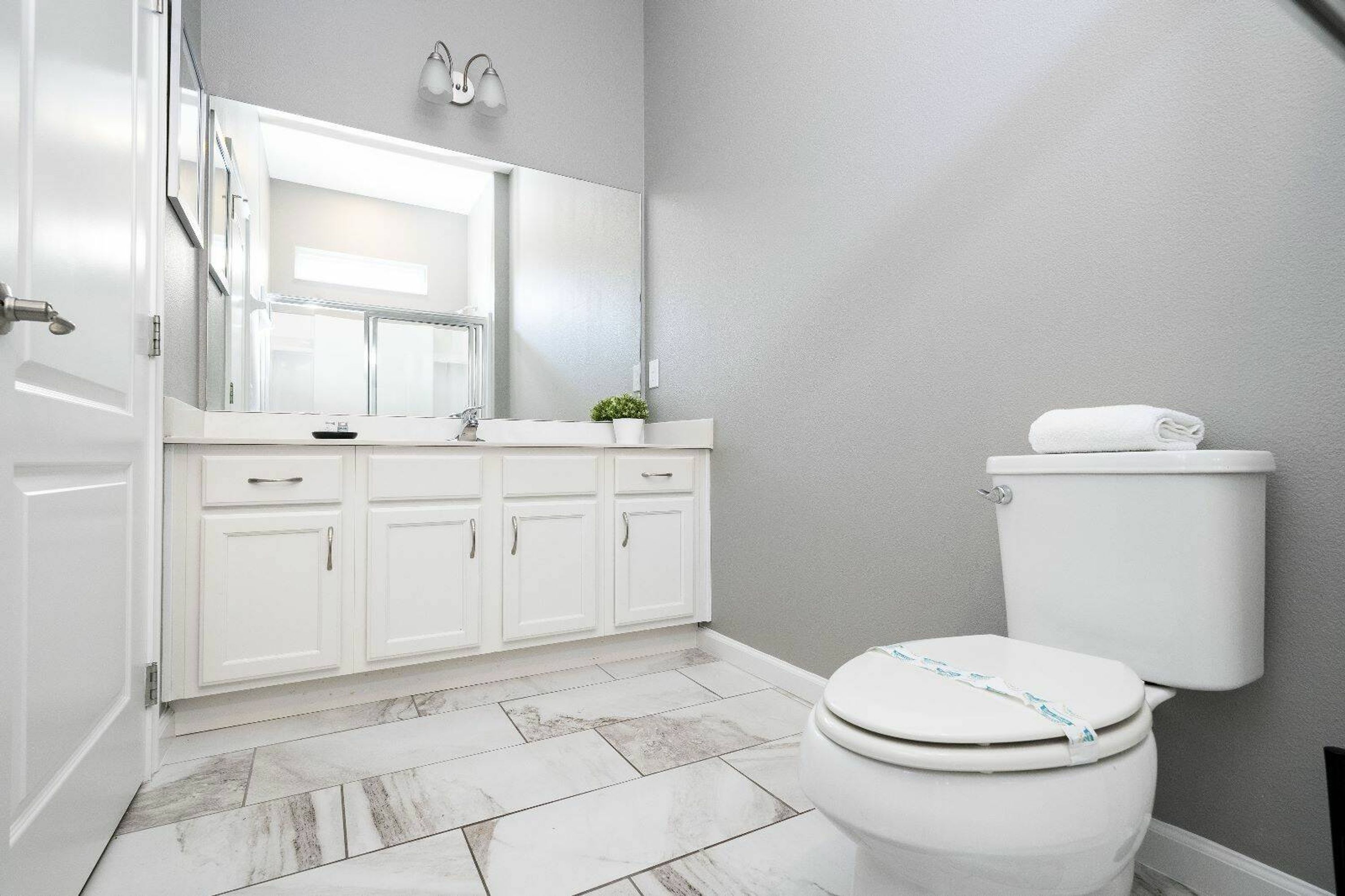 Un bagno con mobili bianchi, un water bianco e uno specchio sopra il lavandino.