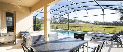 A covered outdoor area with a pool, lounge chairs, and a table.