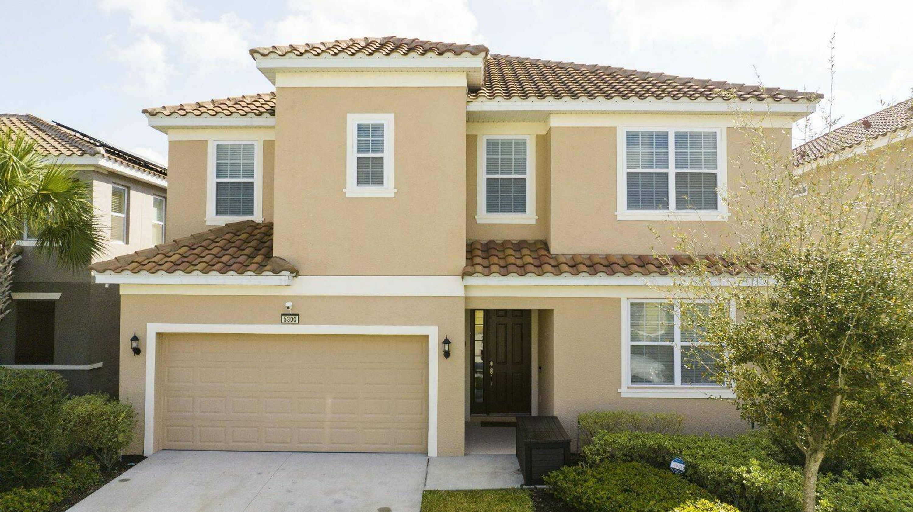 A two-story house with a beige facade, a tiled roof, and a garage.