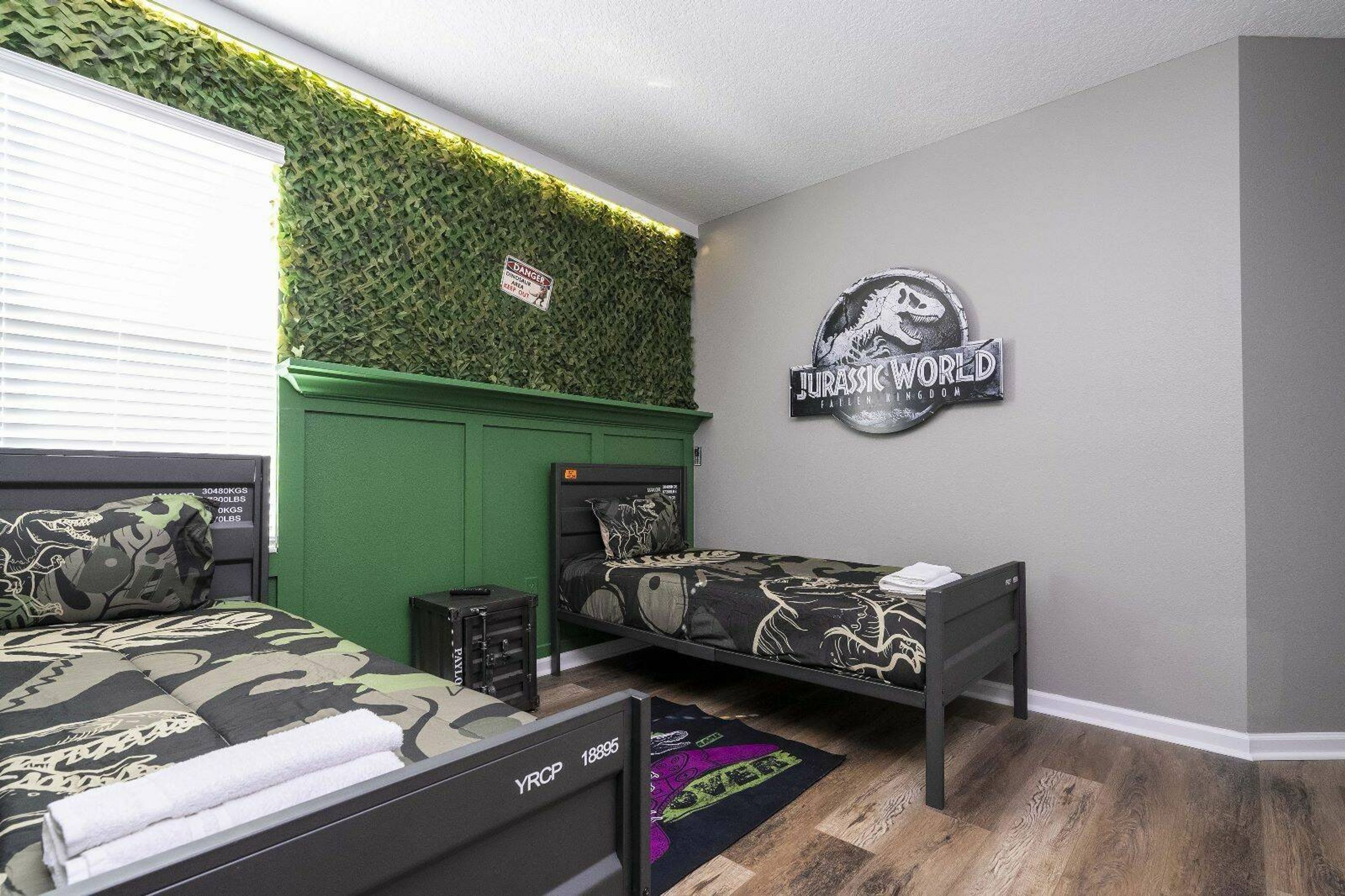 A bedroom with two beds, green walls, a 'Jurassic World Fallen Kingdom' sign, and a green wall with a 'Danger' sign.