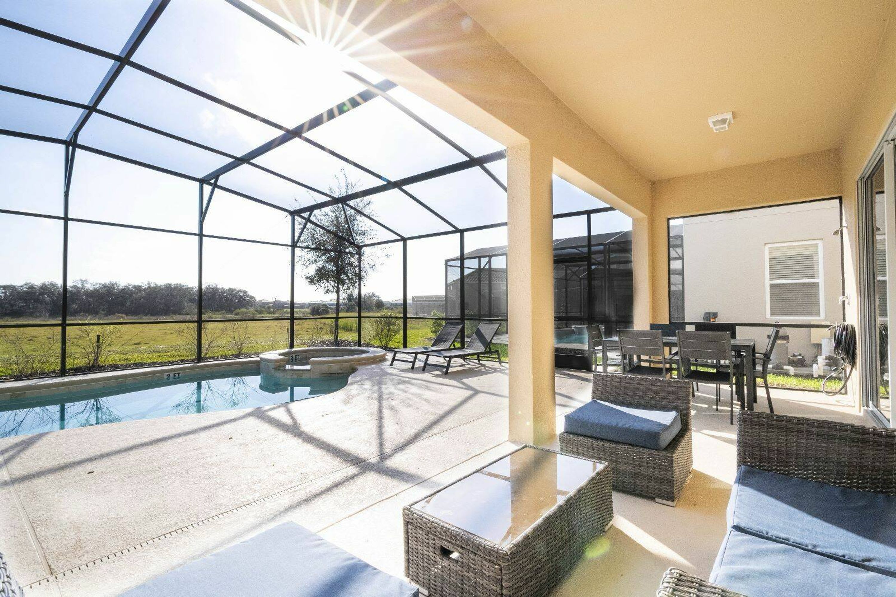 A covered outdoor area with a pool, seating, and a view of the countryside.