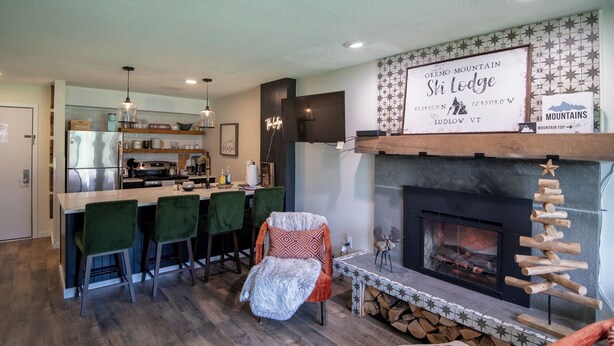 A cozy living room with a fireplace, a bar area, and a kitchen in the background.