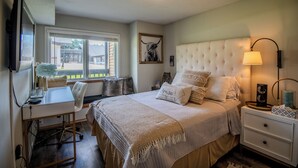 A bedroom with a bed, bedside table, lamp, and a desk with a chair.