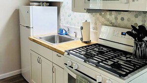 Une cuisine compacte avec des meubles blancs, un évier en acier inoxydable, un four à micro-ondes, une cuisinière et un réfrigérateur.