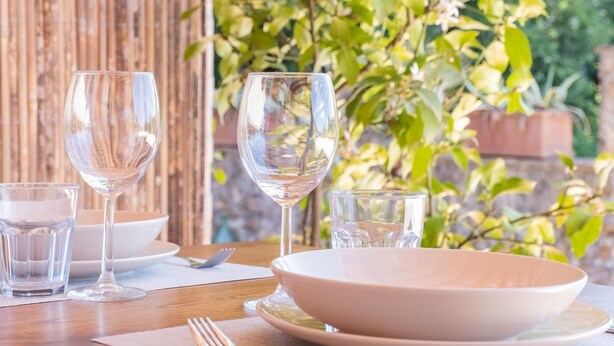 A dining table set outdoors with clear glassware, a bowl, and a plate.