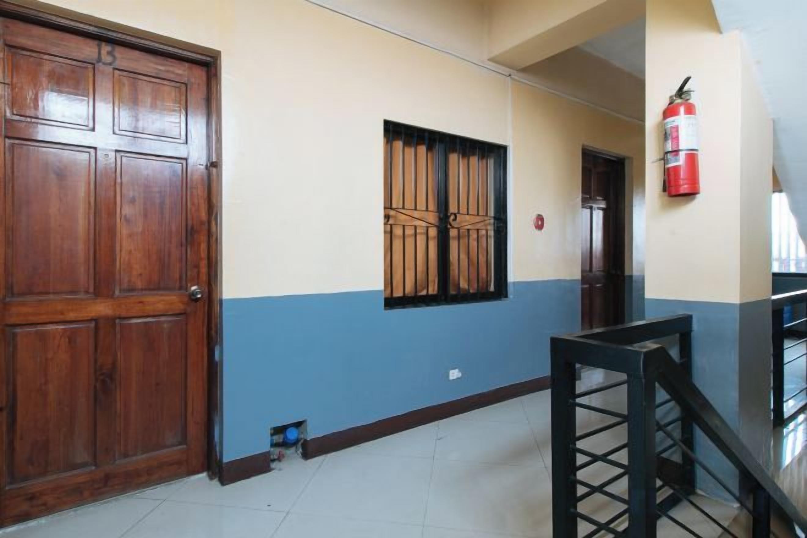 A hallway with a wooden door, a window with bars, a fire extinguisher, and a staircase.