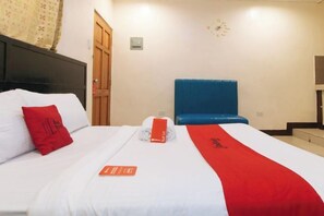 Een hotelkamer met een bed, een rood kussen, een deken in wit en rood, een blauwe hoofdbord en een klok aan de muur.