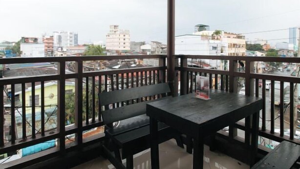 A balcony with a wooden table and bench, offering a view of a cityscape with various buildings. - RedDoorz @ VCat Apartelle Sampaloc Manila (Quezon City)