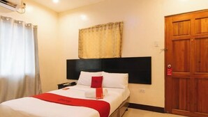 A hotel room with a bed, a nightstand, a wooden door, and a window with curtains. - RedDoorz @ VCat Apartelle Sampaloc Manila (Quezon City)