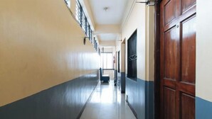 A long, narrow hallway with a blue and beige color scheme, a wooden door on the right, and a window on the left. - RedDoorz @ VCat Apartelle Sampaloc Manila (Quezon City)