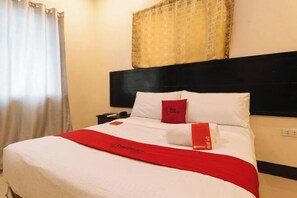 Een hotelkamer met een bed, nachtkastje, rode plaid en een patroon gordijn.