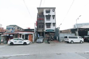 A multi-story building with a storefront on the ground floor, a white van parked in front, and a motorcycle parked to the side. - RedDoorz @ VCat Apartelle Sampaloc Manila (Quezon City)