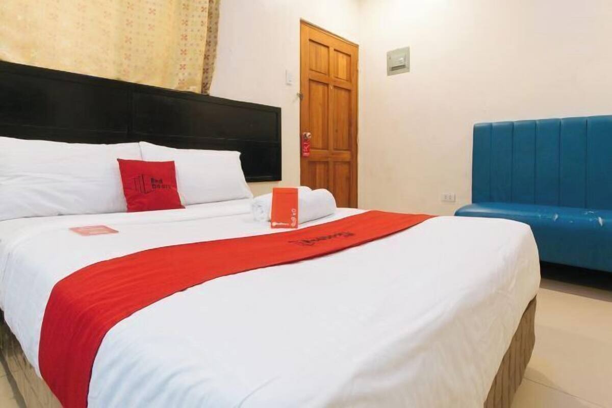 Una habitación de hotel con una cama, una puerta de madera y un banco tapizado en azul.