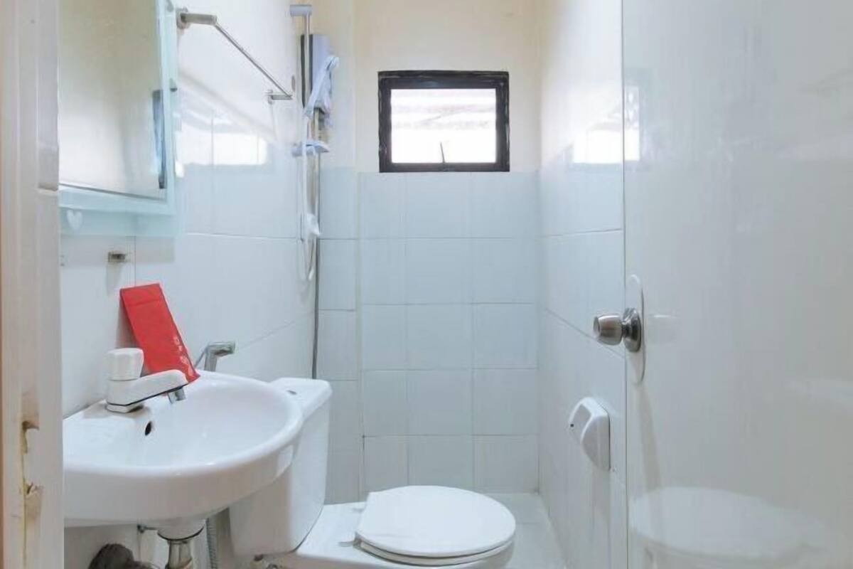 Un baño pequeño y blanco con lavamanos, inodoro y una ventana sobre el inodoro.
