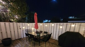 Una terraza de madera con una mesa, sillas, una parrilla y luces colgantes.