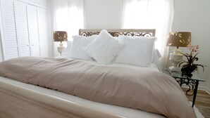 Una cama bien hecha con cabecera de madera, ropa de cama blanca y dos mesitas de noche con lámparas.