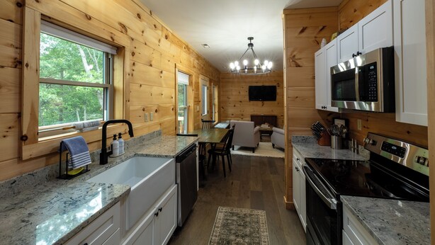 A wooden cabin interior with a kitchen, dining area, and a living room. - The Dam House (Lake Lure)