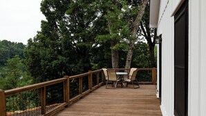 A wooden deck with a table and chairs, surrounded by a white building and trees. - The Dam House (Lake Lure)