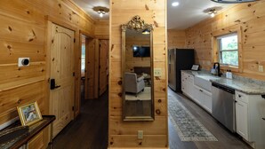 A wooden interior with a large mirror, a kitchen with white cabinets, and a hallway leading to a bedroom. - The Dam House (Lake Lure)