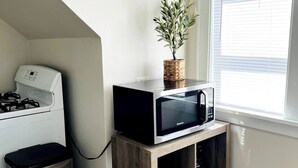 A compact kitchen with a built-in microwave, a small trash bin, a potted plant, and a window with blinds. - 2 Bedroom Near BP Refinery (Hammond)