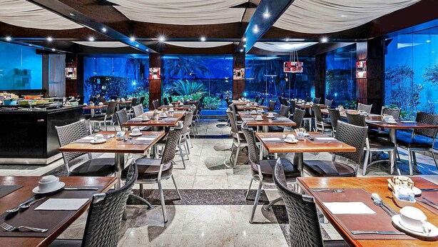 Un ristorante con diversi tavoli e sedie, un grande acquario sullo sfondo e un design d'interni moderno.