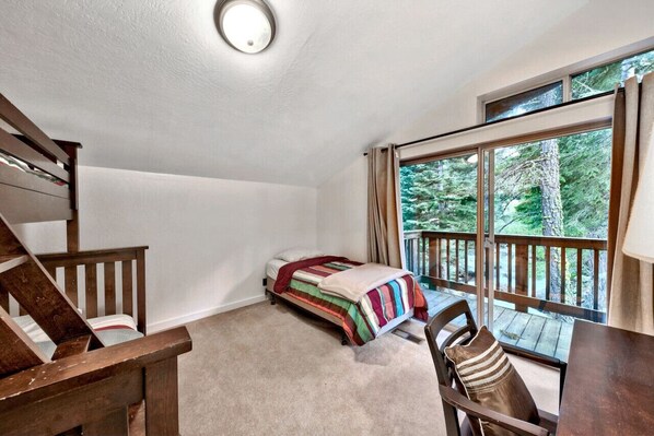 A bedroom with a bed, a chair, a desk, and a window with a view of trees.