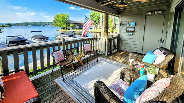 A covered deck with outdoor furniture, a view of the lake, and a dock with boats. - Farr Shores Sunset Serenity (Hot Springs)