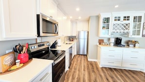 A modern kitchen with white cabinets, stainless steel appliances, a wooden floor, and a built-in wine rack. - Farr Shores Sunset Serenity (Hot Springs)