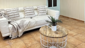 A room with a white leather sofa, a round wooden coffee table, a woven wall hanging, and a door with a light green frame. - Casa Reme, Sencillez y Comodidad Para tu Familia (Playamonte)