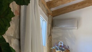 A bedroom with a stone wall, a bed, a window with curtains, a bedside lamp, and a hanging basket with flowers. - Casa Reme, Sencillez y Comodidad Para tu Familia (Playamonte)