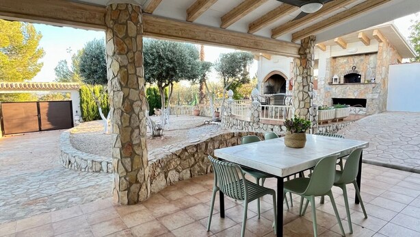 An outdoor patio with stone columns, a stone fireplace, and a table with chairs. - Casa Reme, Sencillez y Comodidad Para tu Familia (Playamonte)