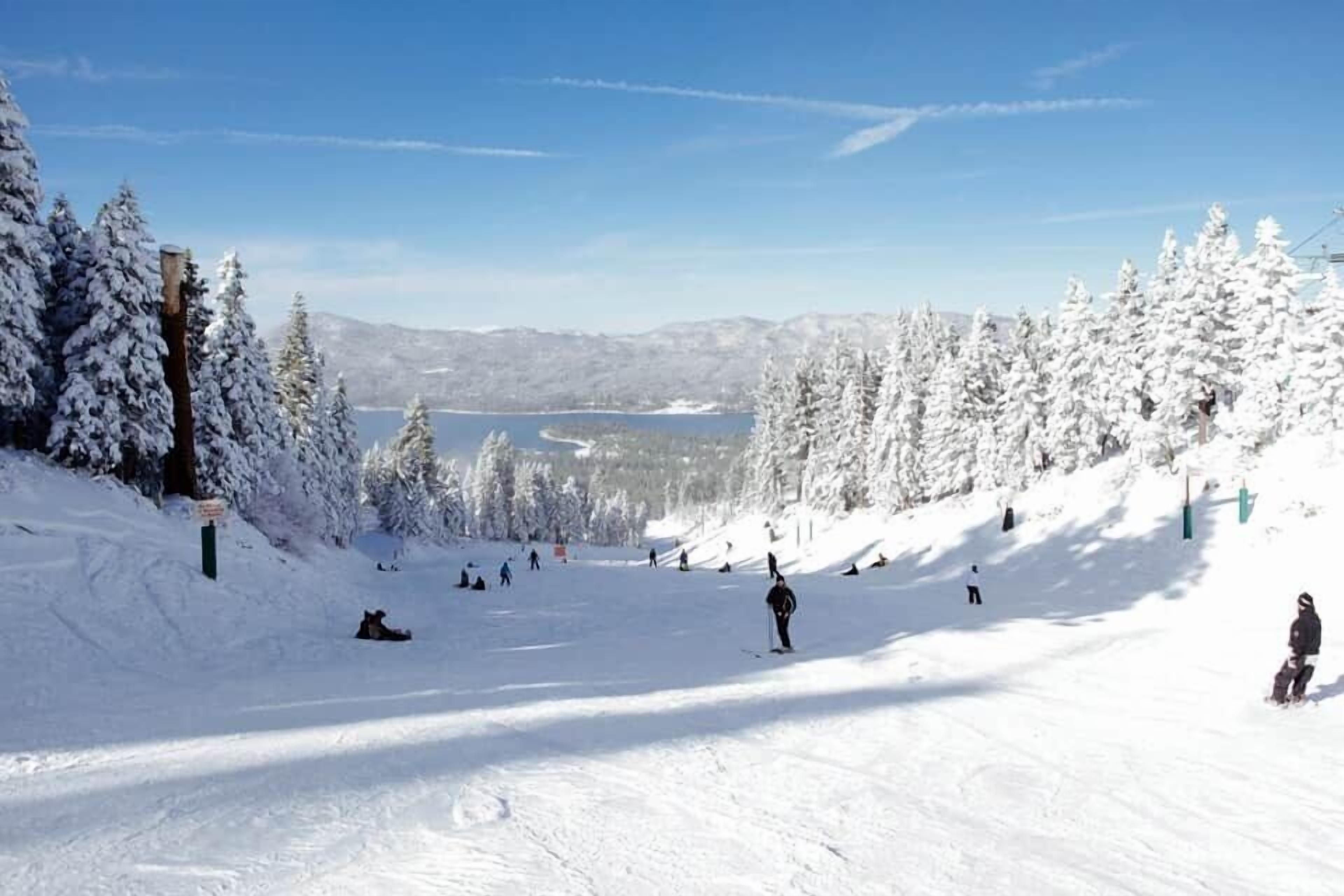 A snowy ski slope with skiers, a lake, and snow-covered trees.