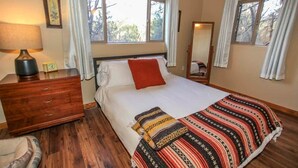 A bedroom with a bed, a wooden dresser, a bedside lamp, a mirror, and windows with curtains. - Overlook Retreat- Awesome Views, Pets Welcome! (Big Bear City)