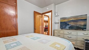 A bedroom with a bed, a dresser, a painting, and a door leading to another room. - On Mountain Time-2bed 1bath+Loft (Big Bear City)