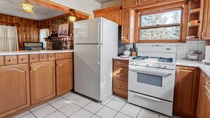 A kitchen with wooden cabinets, a refrigerator, an oven, and a window with a view of trees. - On Mountain Time-2bed 1bath+Loft (Big Bear City)