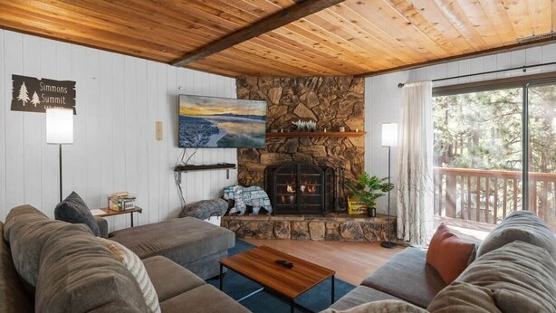 A cozy living room with a stone fireplace, a large sofa, and a wooden ceiling. - Dutch Hideaway-3bed W/Gameroom (Big Bear City)