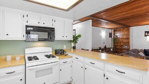 A modern kitchen with white cabinets, a microwave, a stove, and a wooden ceiling. - Dutch Hideaway-3bed W/Gameroom (Big Bear City)