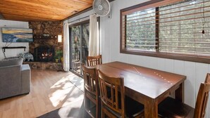 A dining area with a wooden table and chairs, a stone fireplace, and a large window with blinds. - Dutch Hideaway-3bed W/Gameroom (Big Bear City)