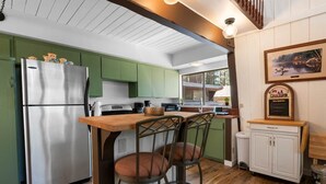 A kitchen with green cabinets, a stainless steel refrigerator, a wooden bar counter, and two bar stools. - Sherwood Cabin-2bed+Loft (Big Bear City)