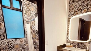 A bathroom with patterned tiles, a window, a mirror, and a sink.