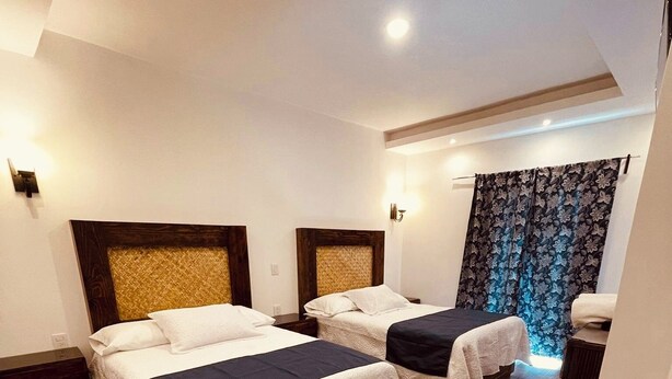 A hotel room with two beds, wooden flooring, and a curtain with a floral pattern.