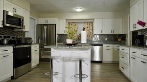 Una cocina moderna con armarios blancos, electrodomésticos de acero inoxidable, una isla central con taburetes de bar y un salpicadero con diseño.