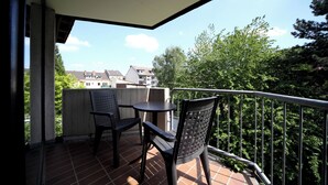 En balkong med ett bord och två stolar, med utsikt över ett bostadsområde med träd och hus.