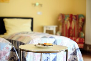 Ein Bett mit floralem Überwurf, ein kleiner Nachttisch und ein Stuhl mit bunten Mustern in einem Zimmer mit gelben Wänden.