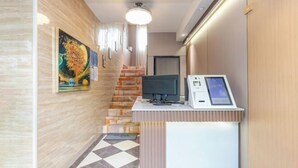 Uma área de recepção com balcão de check-in, um computador e uma escadaria.